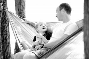 a father and son sit on a hammock