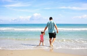 a father and toddler daughter holding hands on the beach